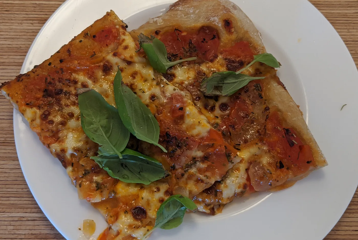 Zwei Stücke Pizza mit Käse, Tomaten und Basilikum auf einem weißen Teller