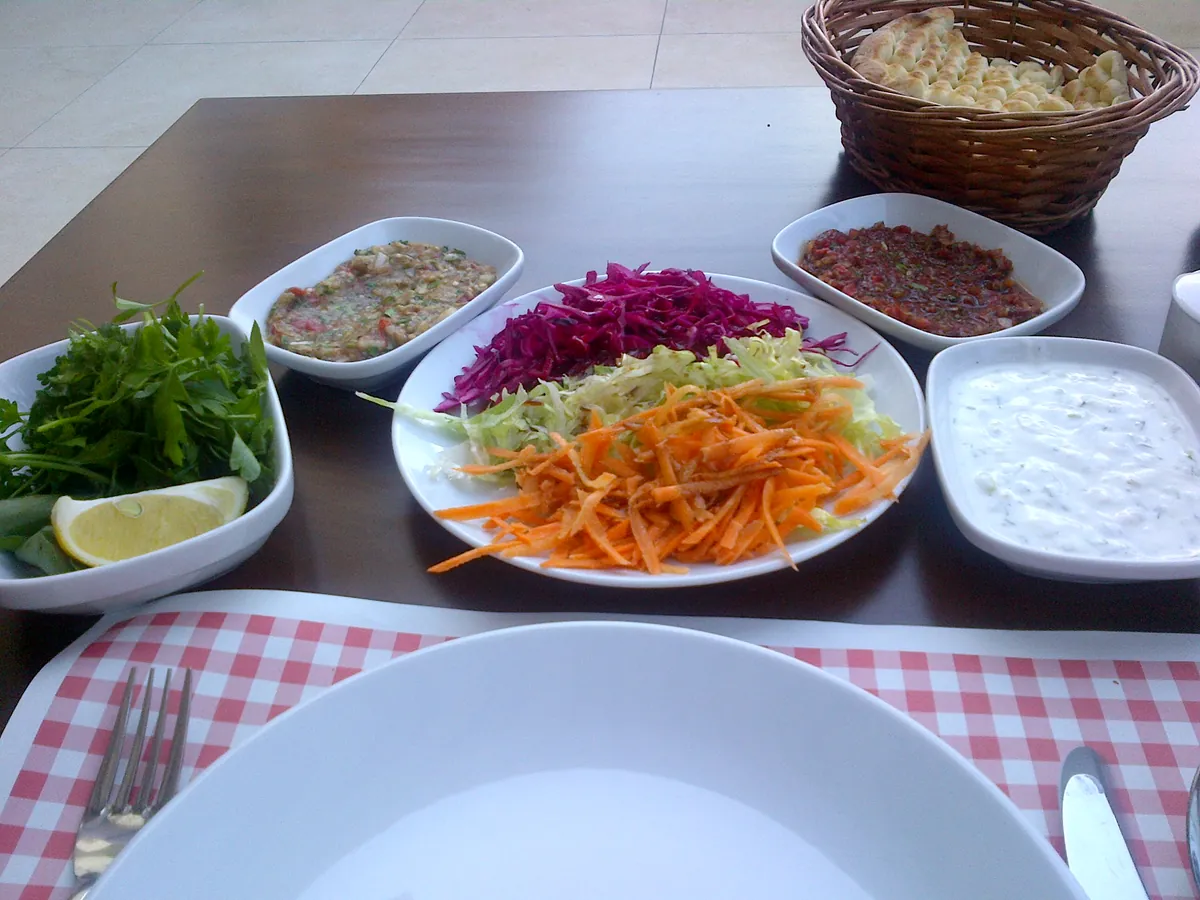 Mehrere Schälchen mit Dips, Salat und Kräutern neben einem Brotkorb auf einem Tisch