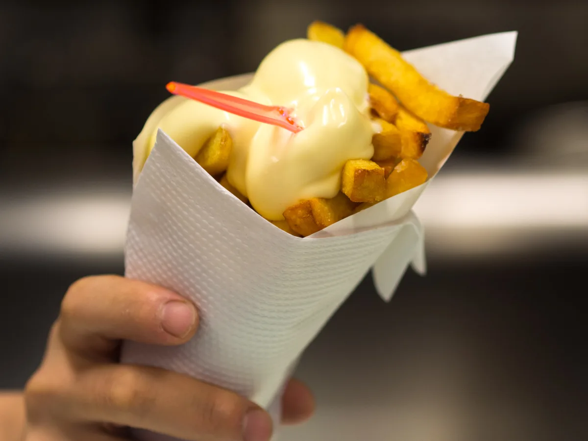 Pommes frites mit Mayonnaise in einer Papiertüte, in der Hand gehalten
