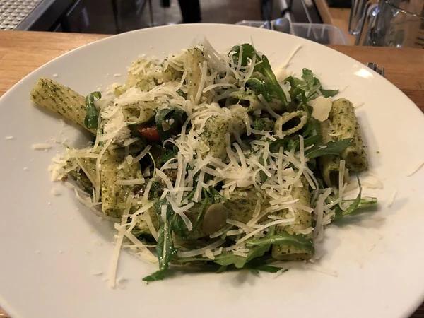 Pasta mit Pesto, Rucola und geriebenem Hartkäse auf weißem Teller