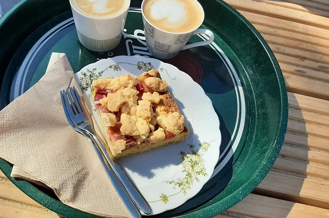 Tablett mit Streuselkuchen und zwei Cappuccino auf einem Holztisch im Garten