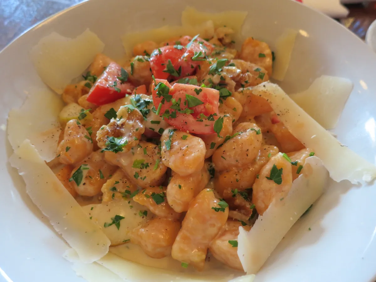 Gnocchi in heller Sauce mit Tomatenstücken, Kräutern und Käsespänen in einer weißen Schale