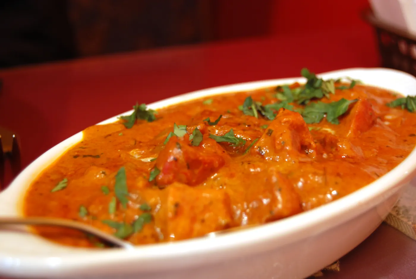 Ovale Schale mit Currysauce, Fleischstücken und Korianderblättern