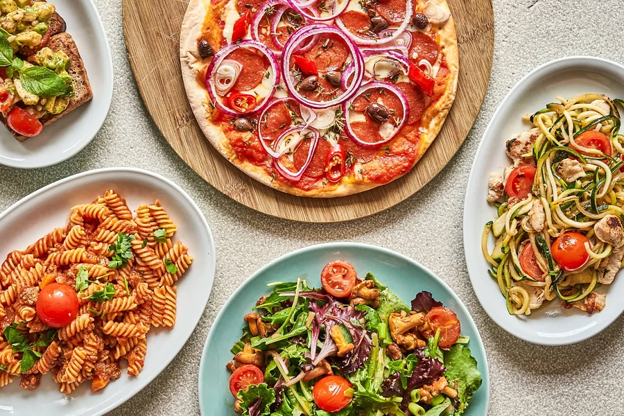 Tisch mit Pizza, Pasta, Zucchini-Spaghetti und Salat von oben fotografiert