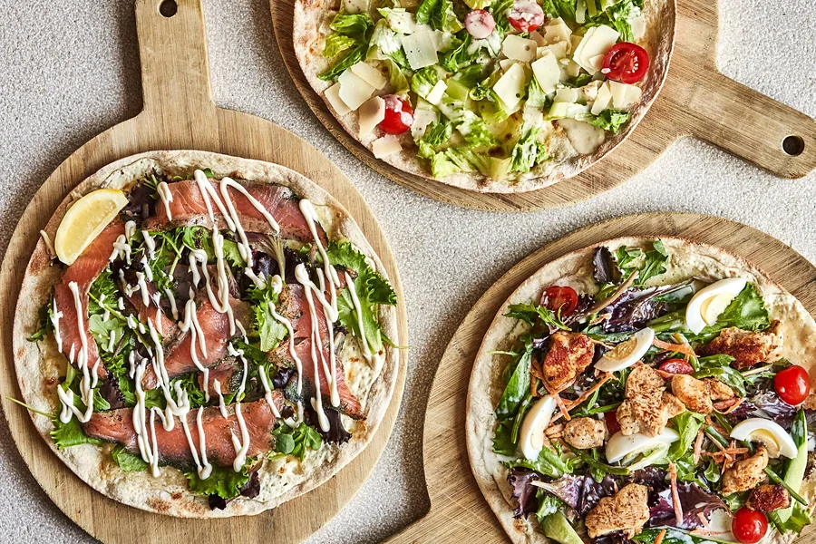 Drei Pizza Fina mit Rohschinken, Rucola, Käse und Salatbelag auf Holzbrettern