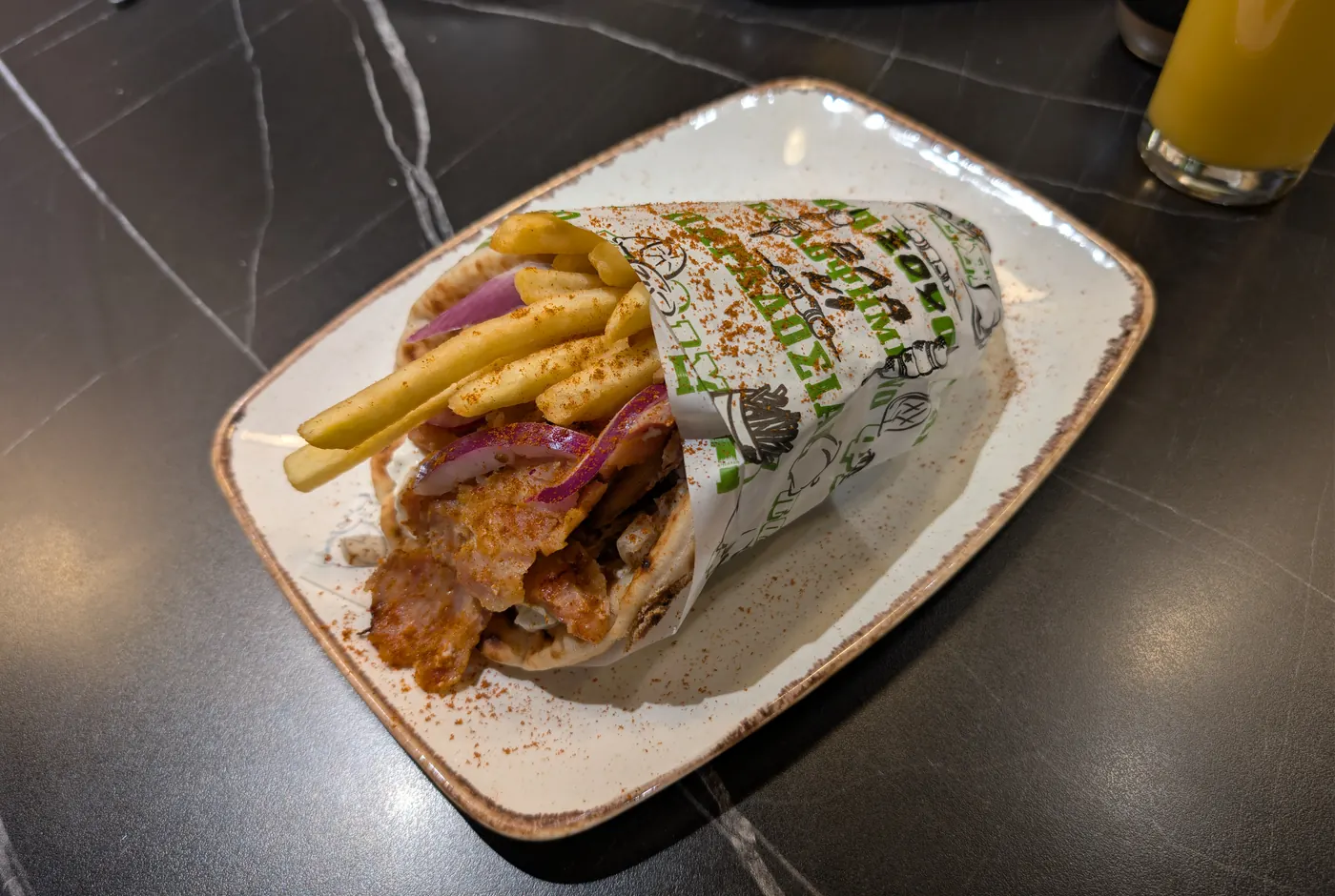 Gefüllte Pita mit Gyros, Pommes und roten Zwiebeln in Papier gewickelt