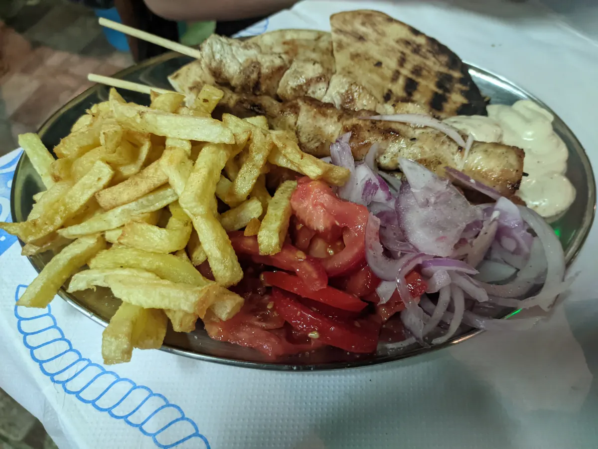 Teller mit Hähnchenspießen, Pommes, Tomaten, Zwiebeln und Fladenbrot