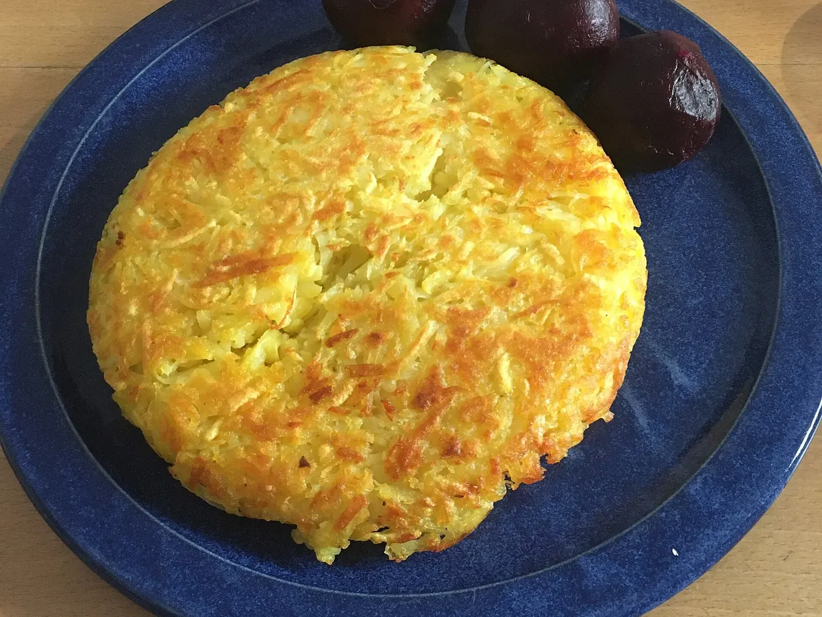 Goldbraun gebratene Rösti auf einem blauen Teller, daneben eingelegte rote Bete