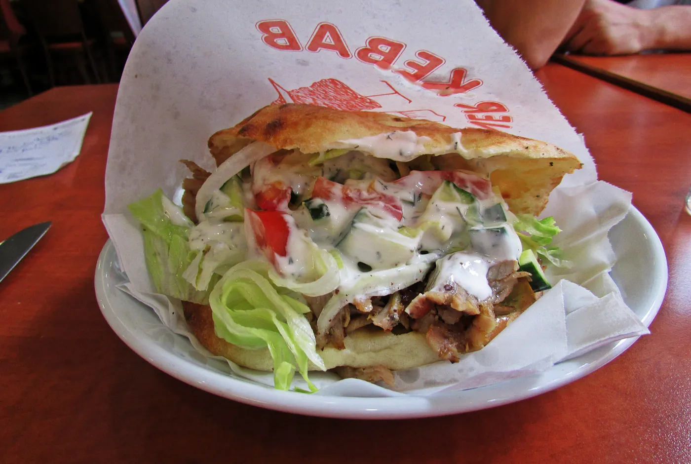 Döner im Fladenbrot mit Fleisch, Salat, Zwiebeln, Tomate und heller Sauce auf einem Teller