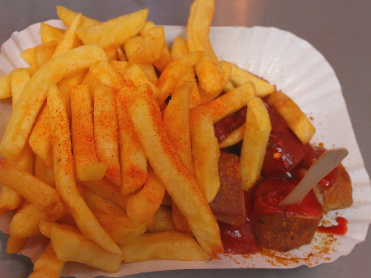 Currywurst in Scheiben mit Currysauce, dazu eine Portion Pommes frites auf einem Pappteller