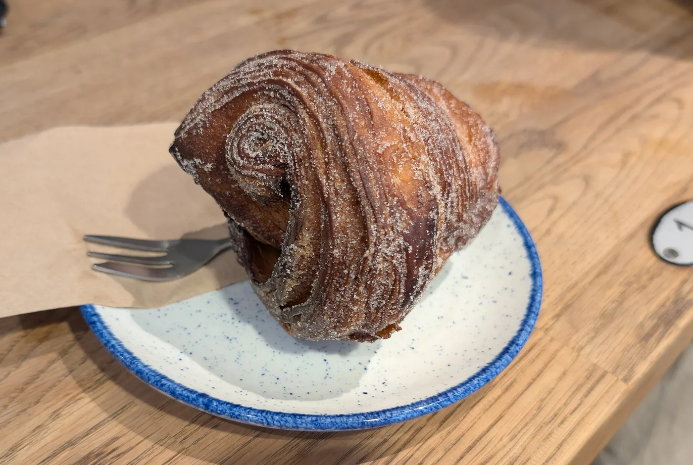 Zimtschnecke in Zimtzucker auf einem blau geränderten Teller auf hellem Holztisch