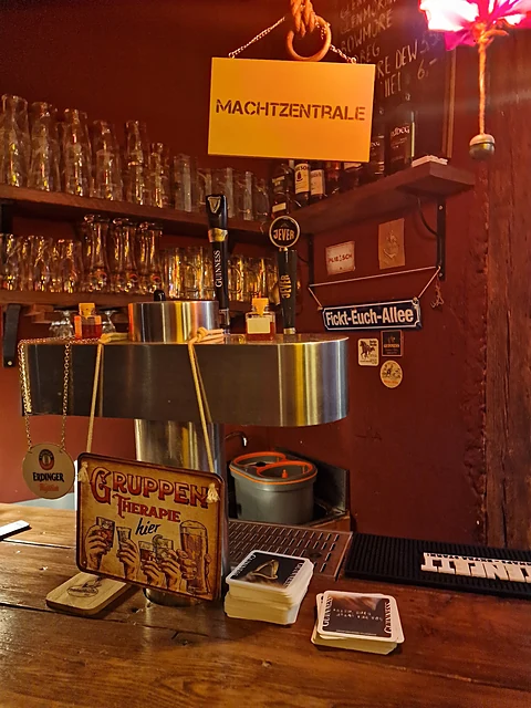 Tresen mit Zapfanlage, Gläserregal, Schild Machtzentrale und Bierdeckeln, rote Wände
