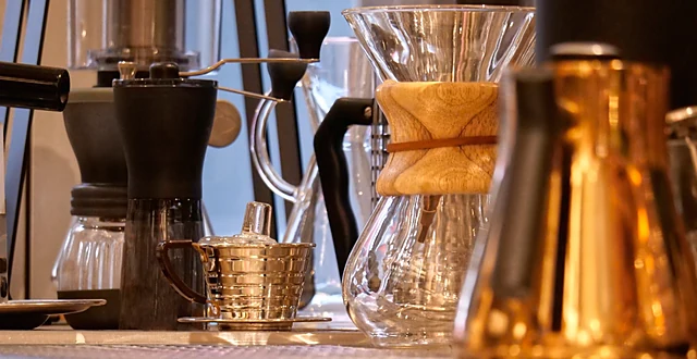 Chemex-Kanne mit Papierfilter, Kupferkännchen und Gläser auf dem Holztresen der Brew-Bar