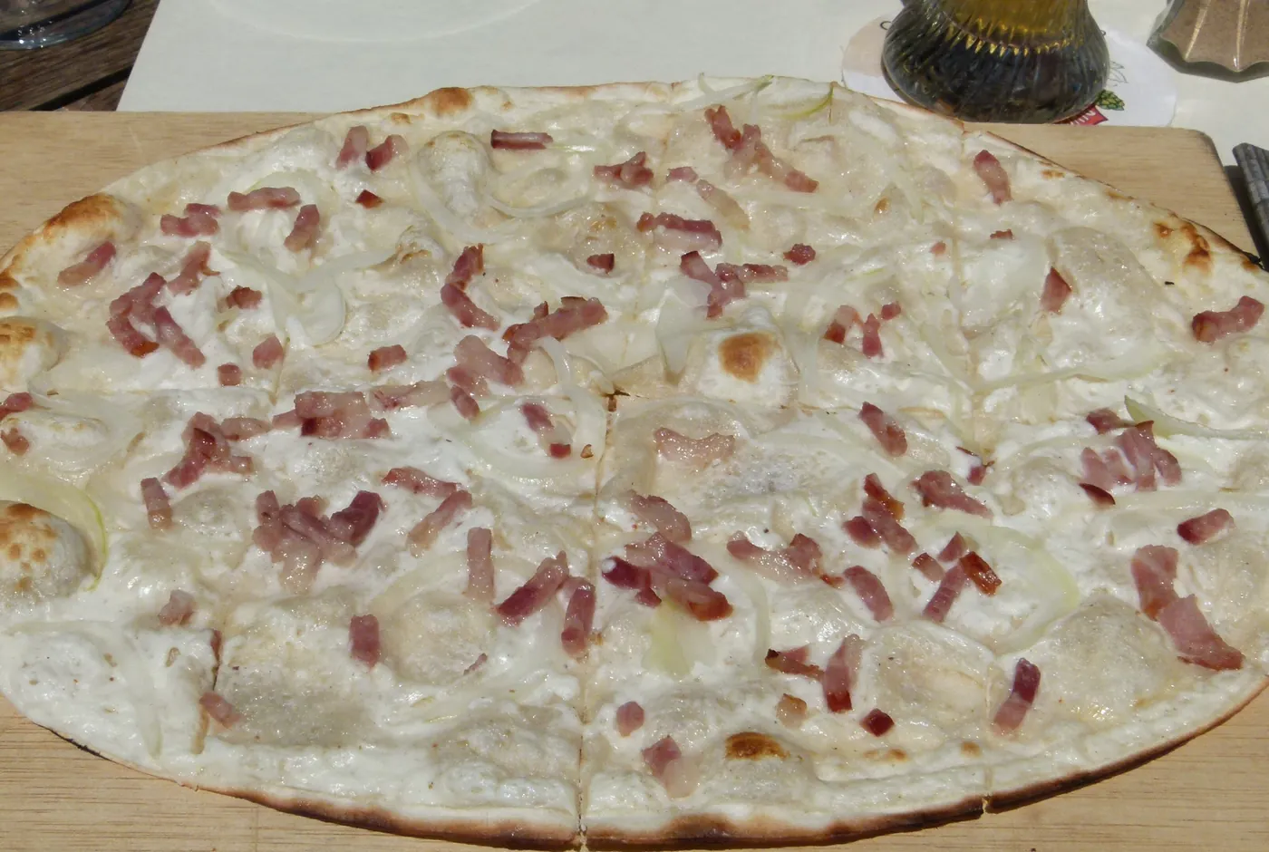 Flammkuchen mit Speckwürfeln und Zwiebeln auf einem Holzbrett