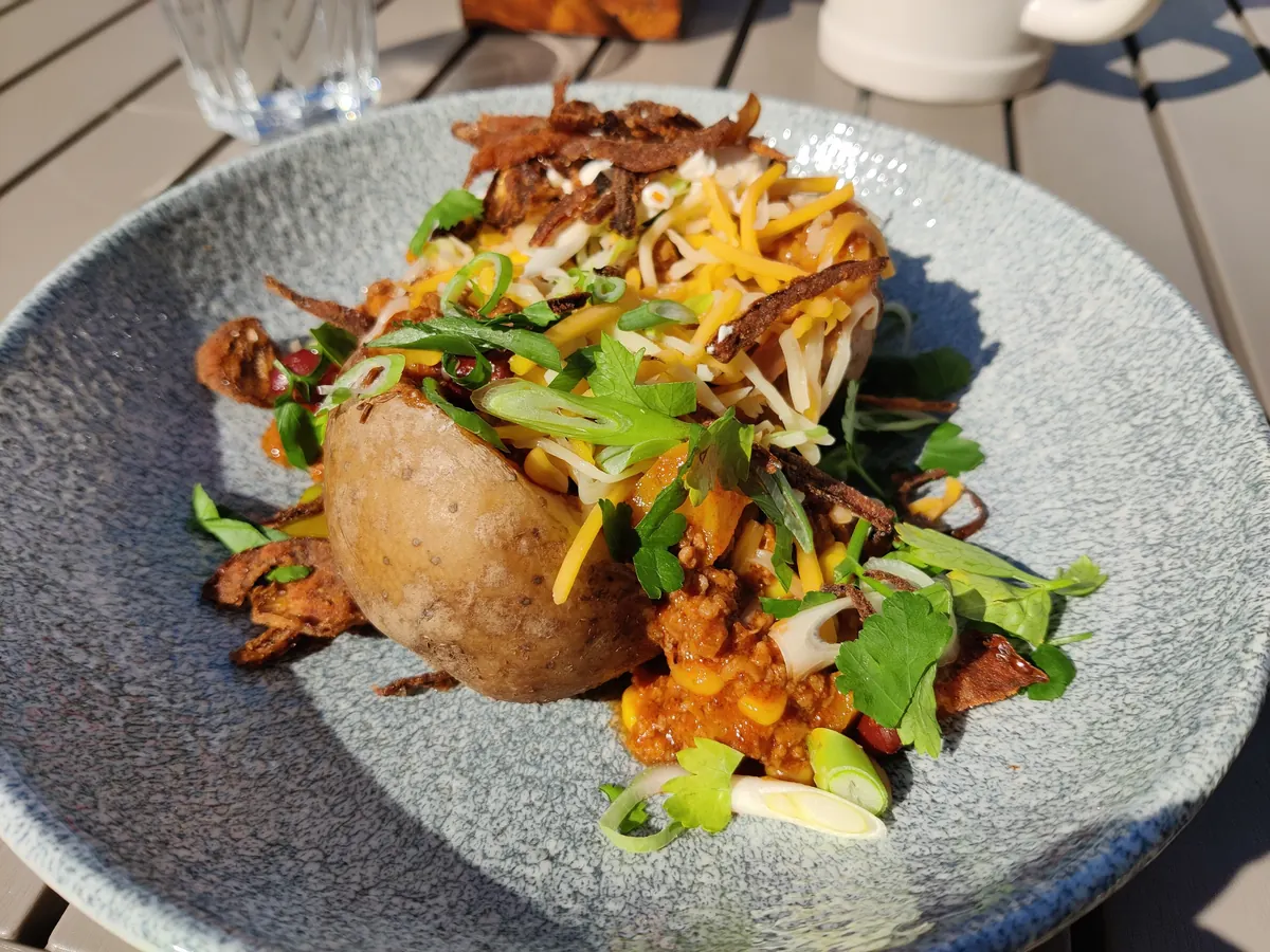 Aufgeschnittene Ofenkartoffel, gefüllt mit Chili con Carne, geriebenem Käse und Sauerrahm