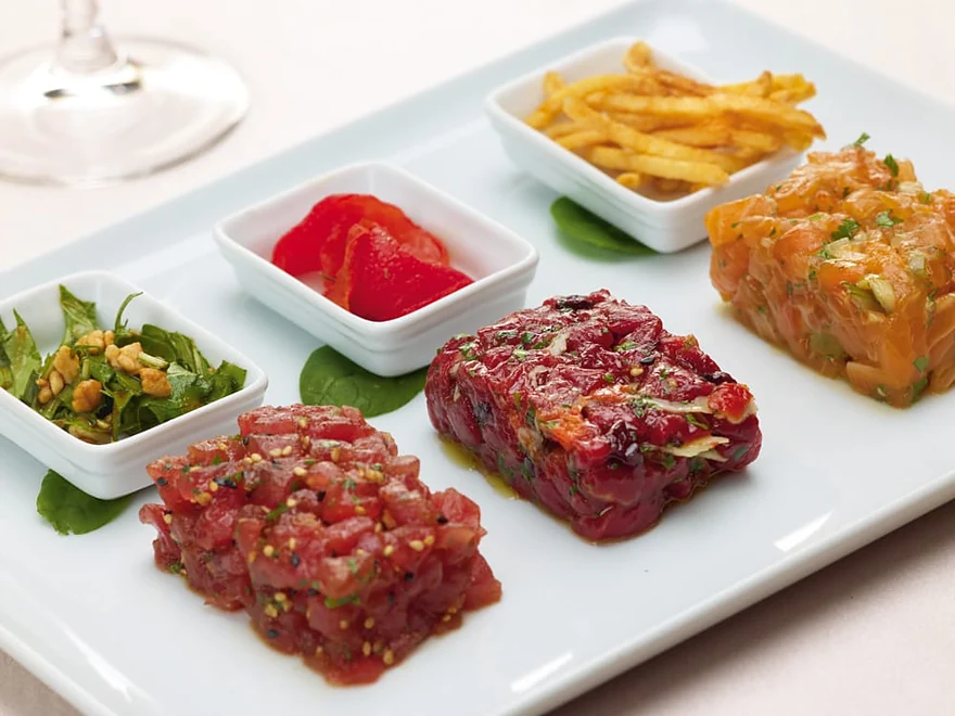 Tatar-Variation mit drei Sorten Tatar, Pommes Allumettes und Beilagen auf länglichem Teller