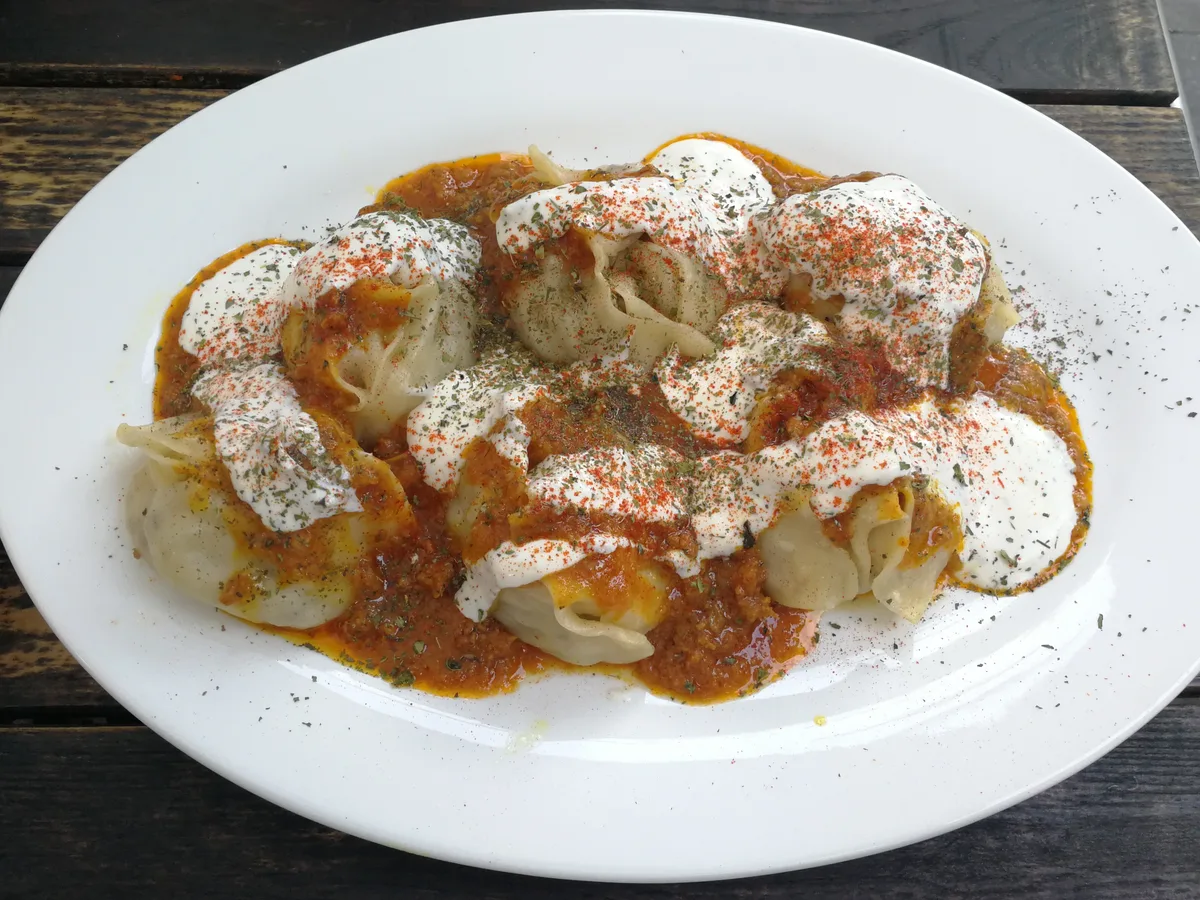 Dampfgegarte Teigtaschen mit Joghurt und Tomaten-Hackfleischsauce auf einem Teller