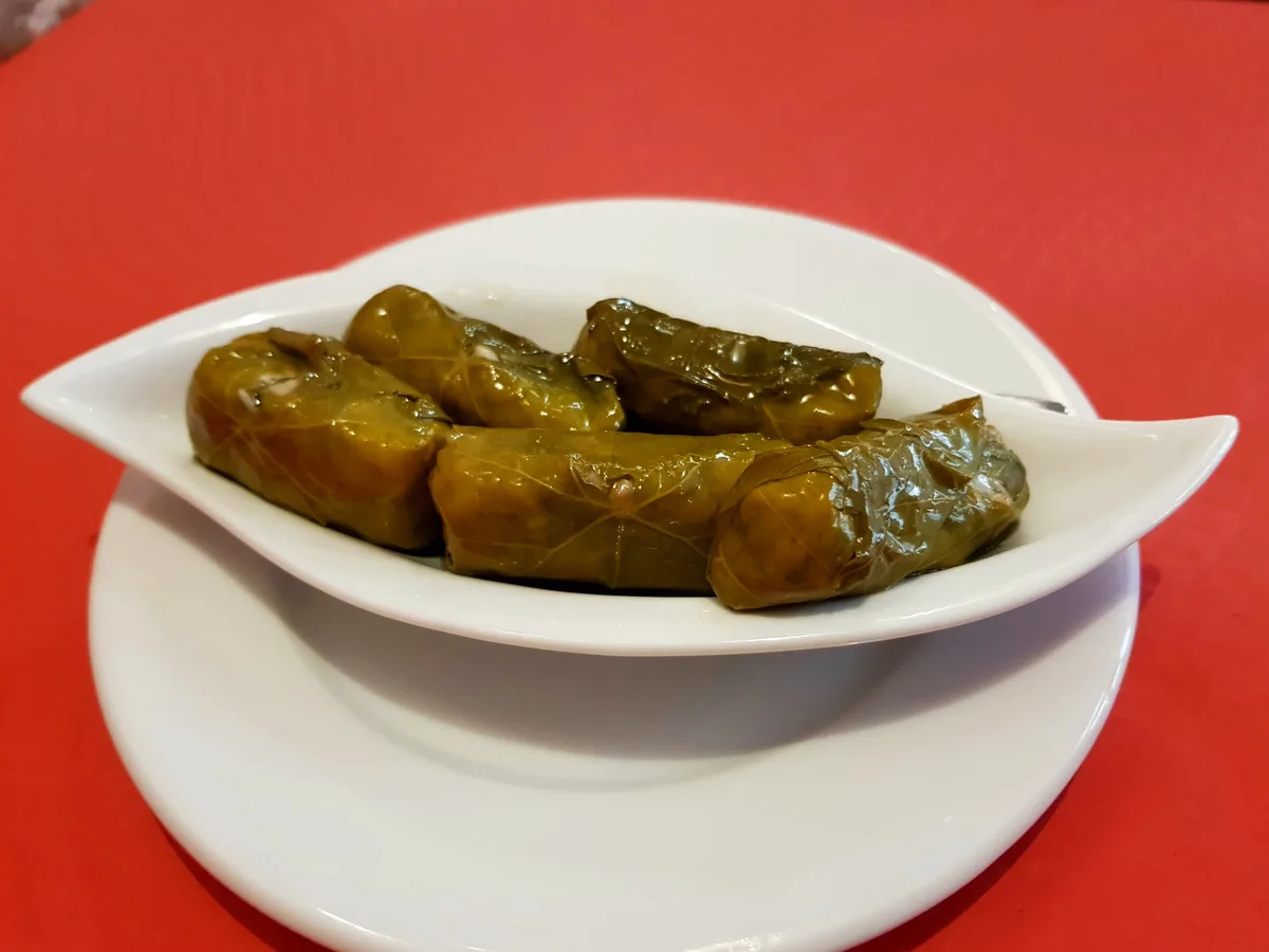 Gefüllte Weinblätter in einer weißen Schale auf rotem Tisch