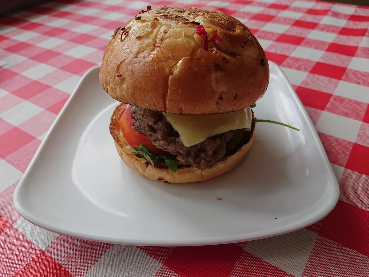 Cheeseburger mit Rindfleisch, geschmolzenem Käse, Tomate und Rucola auf einem weißen Teller