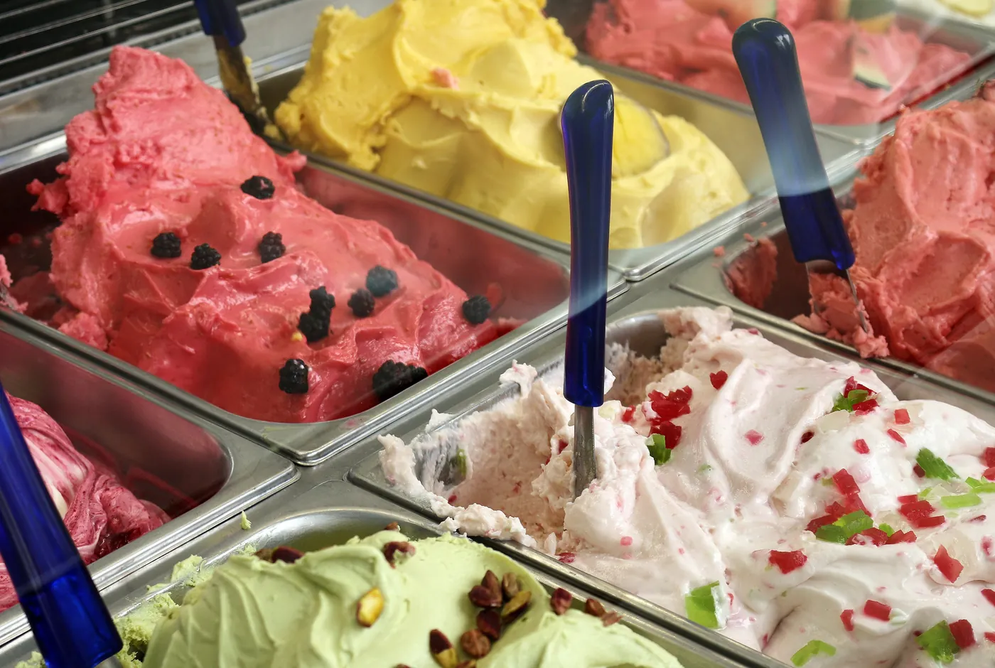 Behälter mit Eis in vielen Sorten in einer Eistheke, dazwischen blaue Portionierer