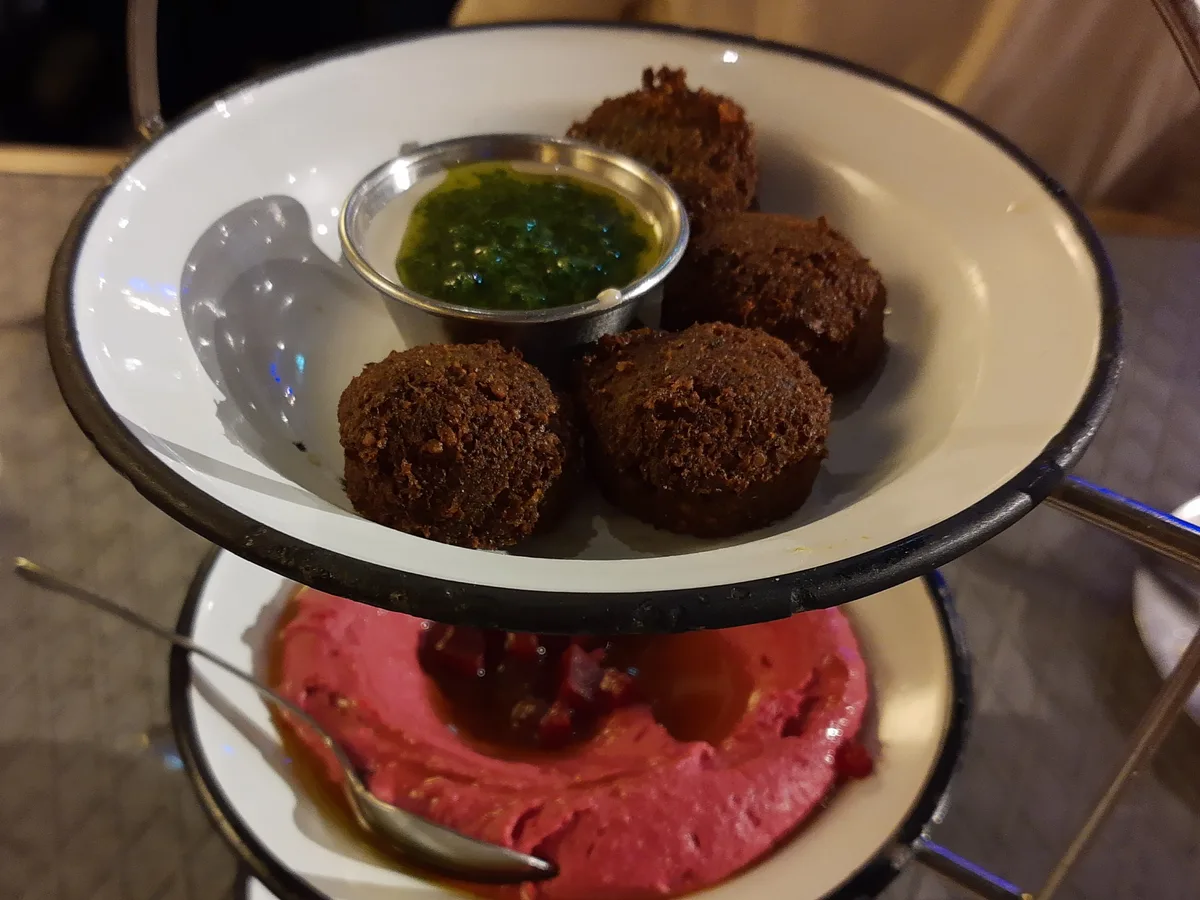 Falafelbällchen mit grüner Zhug-Sauce, darunter eine Schale mit rotem Hummus