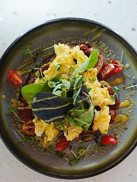 Rührei-Stulle mit Kirschtomaten, Kresse und Kernen auf einem dunklen Teller, von oben