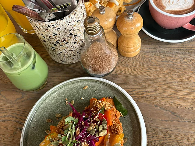 Bunte Veggie-Stulle mit mariniertem Gemüse und Sprossen in einer grauen Schale, dahinter Cappuccino, Matcha und Gewürzmü