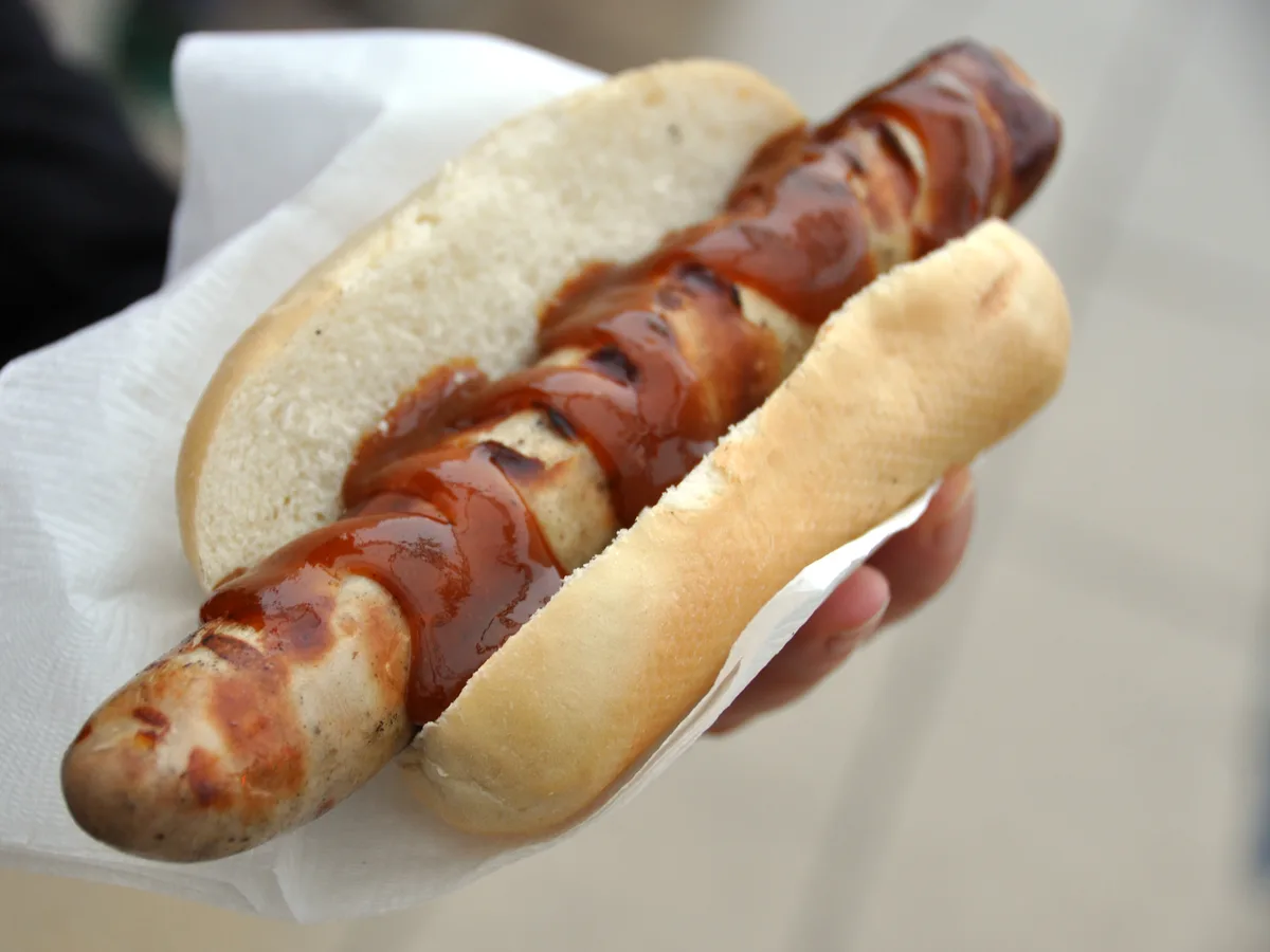 Gegrillte Bratwurst im Brötchen mit Ketchup, in der Hand gehalten