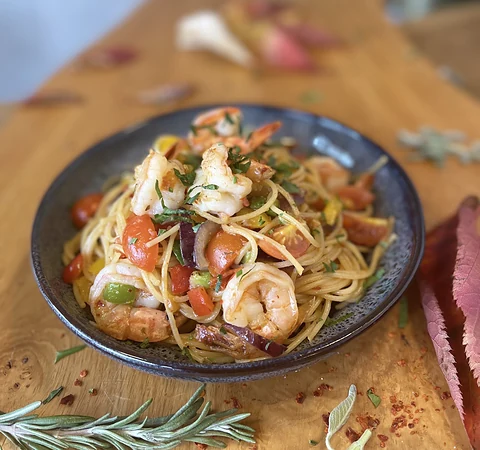 Spaghetti mit Garnelen, Tomaten und Kräutern in dunkler Schale auf Holztisch