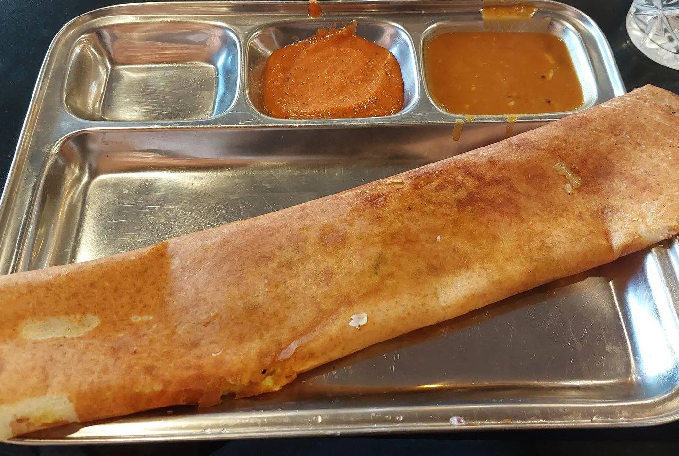 Gerollte Masala Dosa auf einem Edelstahlteller, daneben Chutney und Sambar in kleinen Mulden