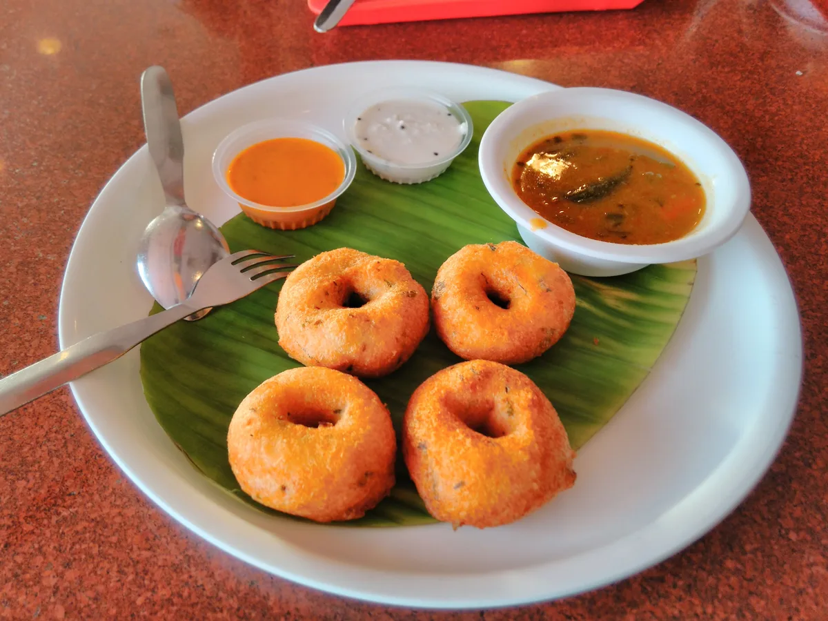Vier Medhu Vada auf einem Bananenblatt, dazu Chutneys und eine Schale Sambar