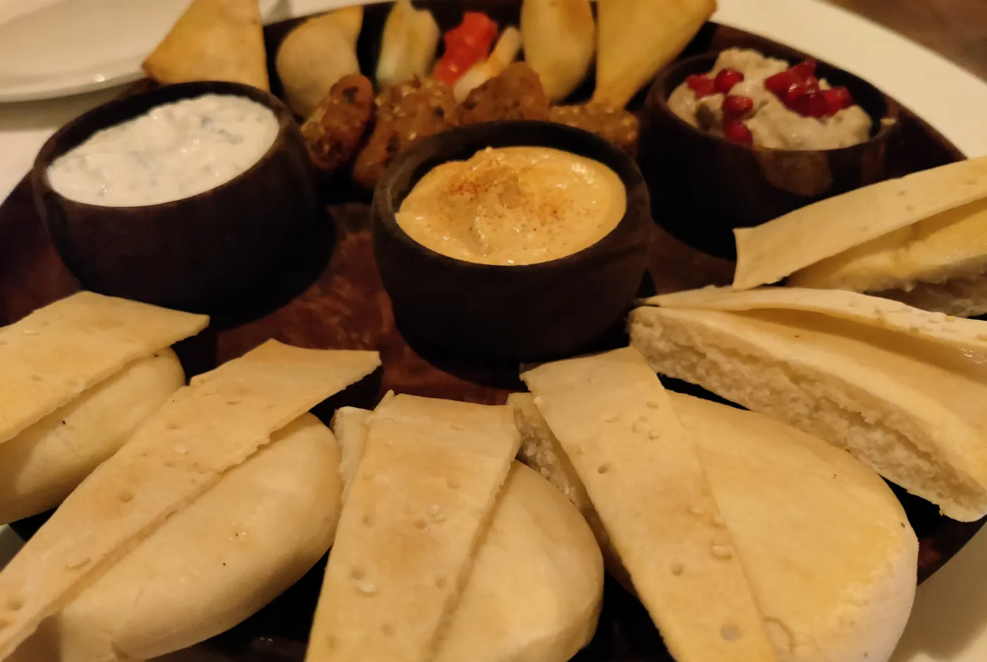 Holzplatte mit Dips in kleinen Schalen, Teigtaschen, Bällchen und aufgeschnittenem Fladenbrot