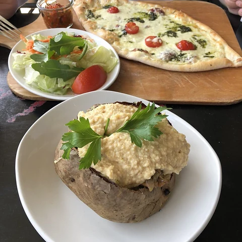 Kumpir, eine gefüllte Ofenkartoffel mit Käse und Petersilie, dahinter Salat und eine Pide