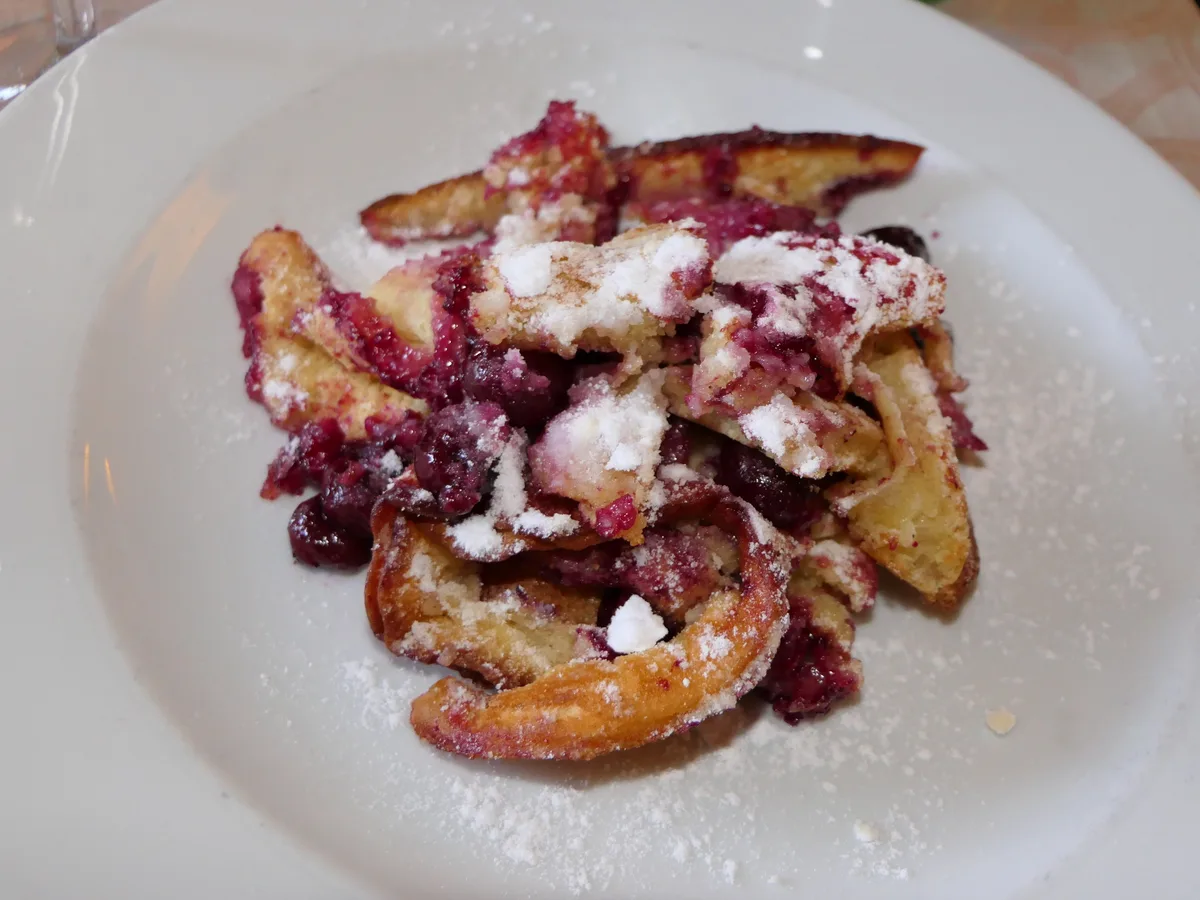 Kaiserschmarrn mit Kirschen und Puderzucker auf einem weißen Teller