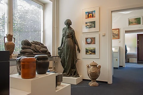 Ausstellungsraum mit historischen Urnen, Bronzestatuen und gerahmten Bildern an den Wänden