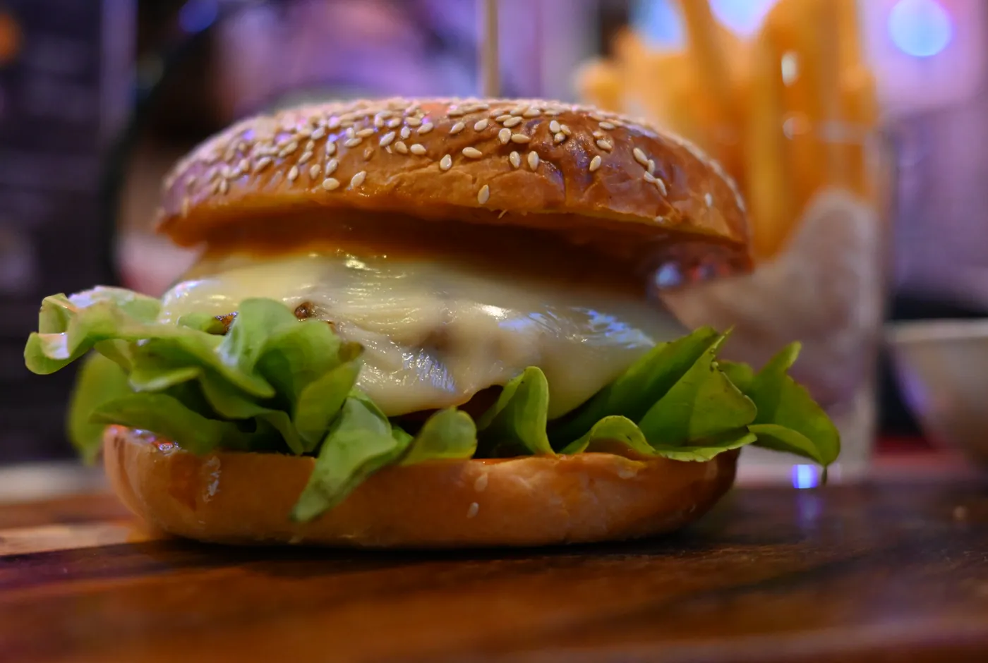 Cheeseburger mit Salat auf einem Sesambrötchen, dahinter ein Körbchen Pommes