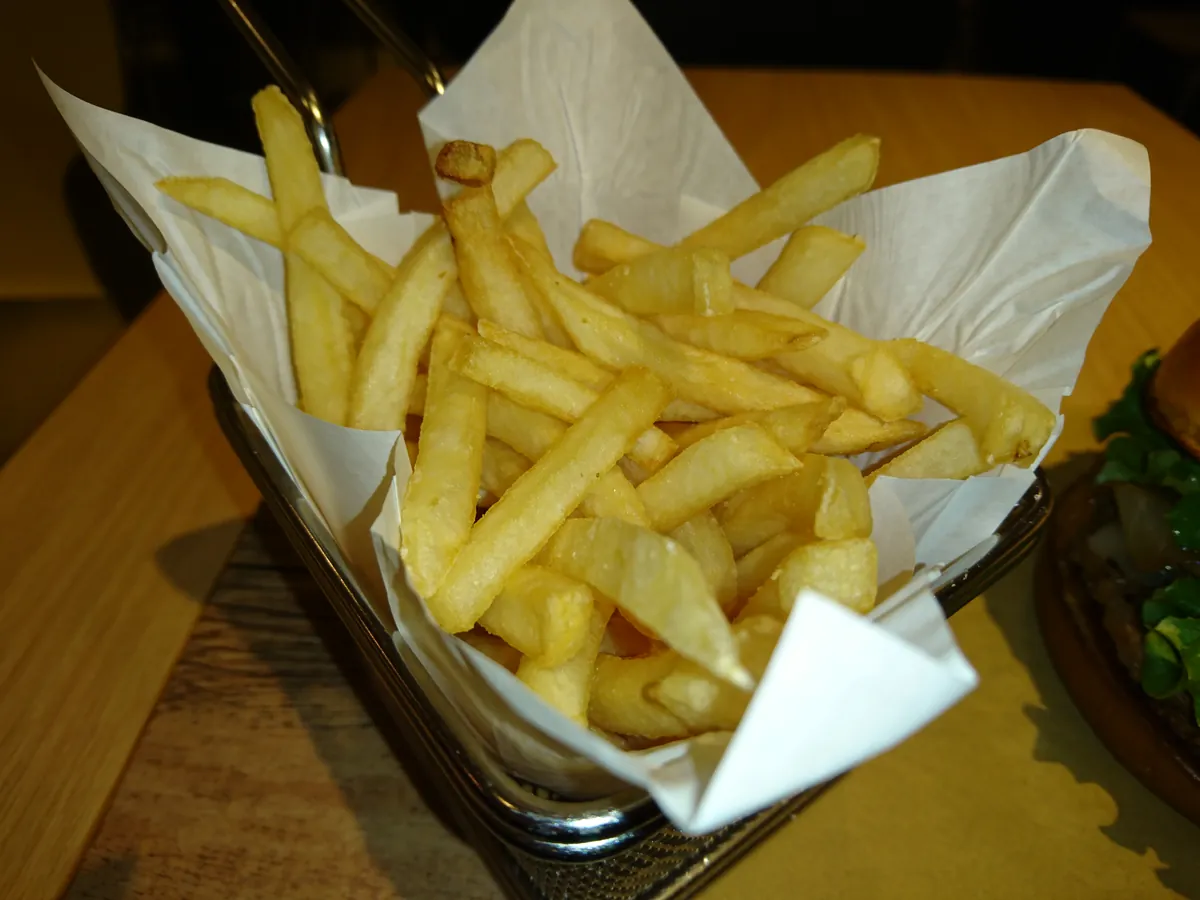 Pommes frites in einem Drahtkörbchen mit Papier auf einem Holztisch