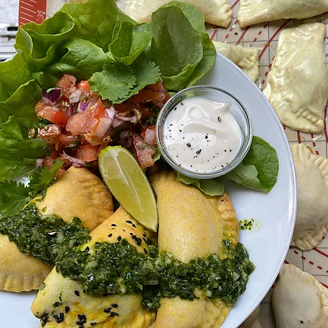 Gebackene Teigtaschen mit grüner Kräutersauce, Tomatensalsa, Limette und Dip auf einem weißen Teller