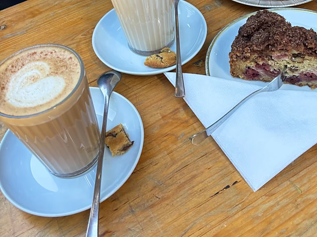 Zwei Latte macchiato in Gläsern und ein Stück Streuselkuchen mit Beeren auf einem Holztisch