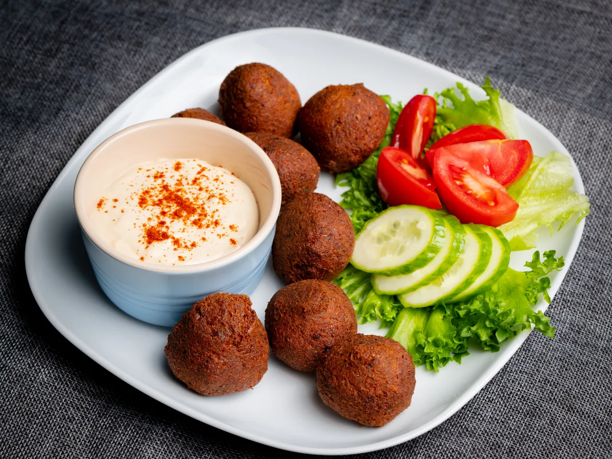 Falafelbällchen mit Tahini-Dip, Tomate und Gurke auf einem weißen Teller