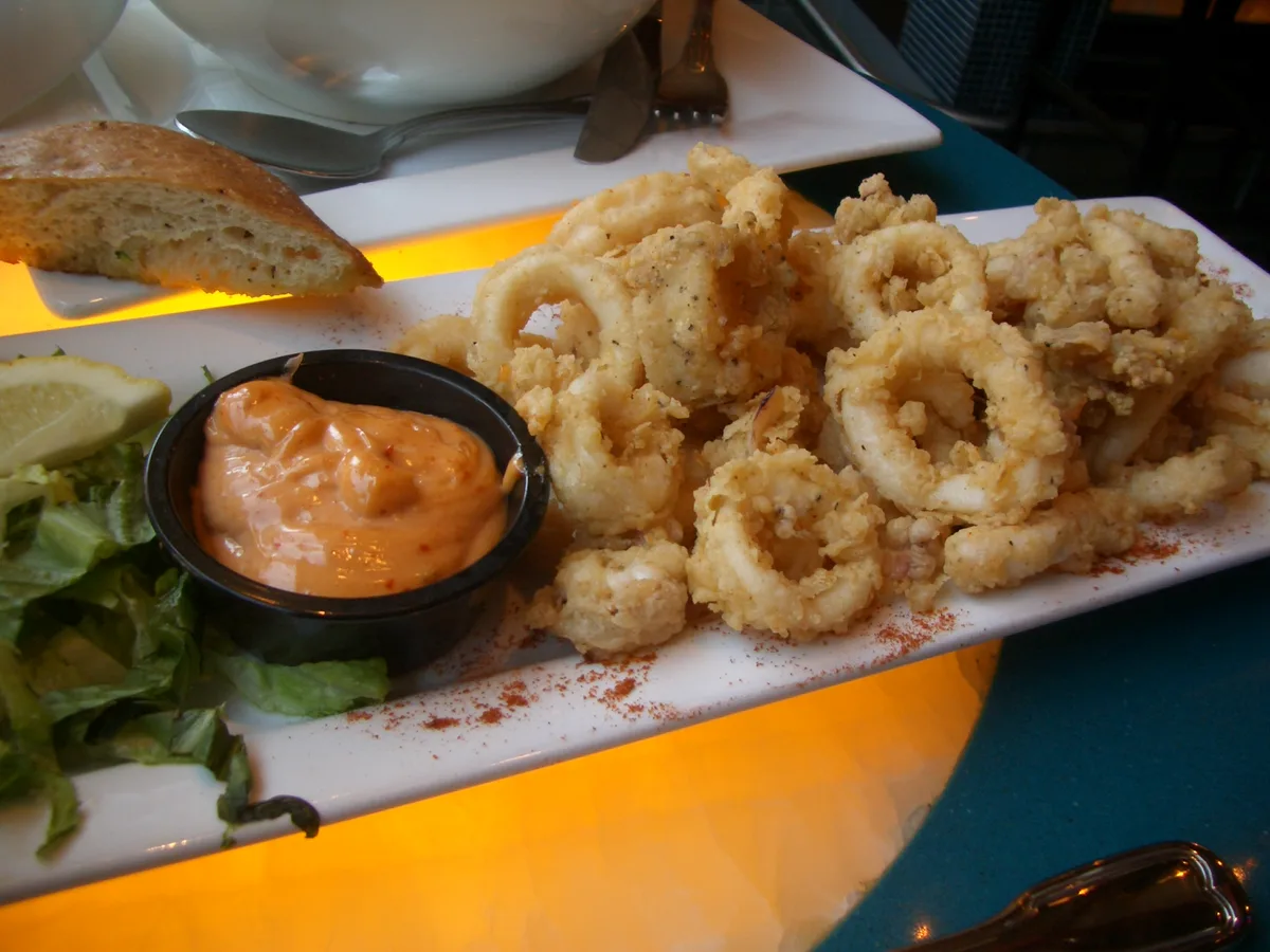 Frittierte Calamari-Ringe mit Zitrone und Dip auf einem weißen Teller