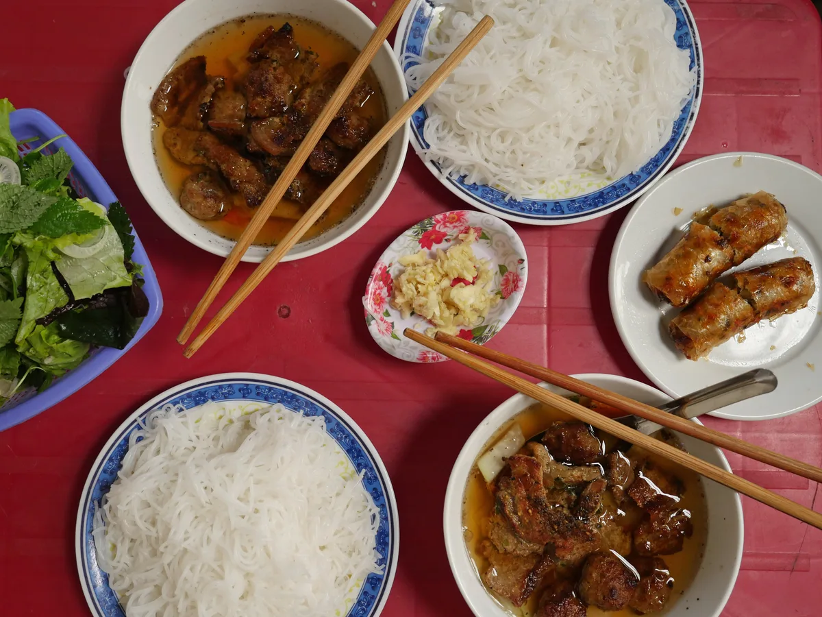 Bun Cha mit gegrilltem Schweinefleisch, Reisnudeln, Frühlingsrollen und frischen Kräutern