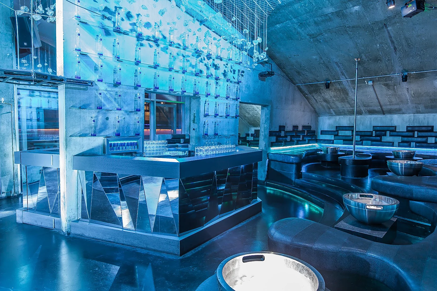 Blau beleuchtete Bar im NOHO Club mit verspiegeltem Tresen, Sitzgruppen und Sektkühler