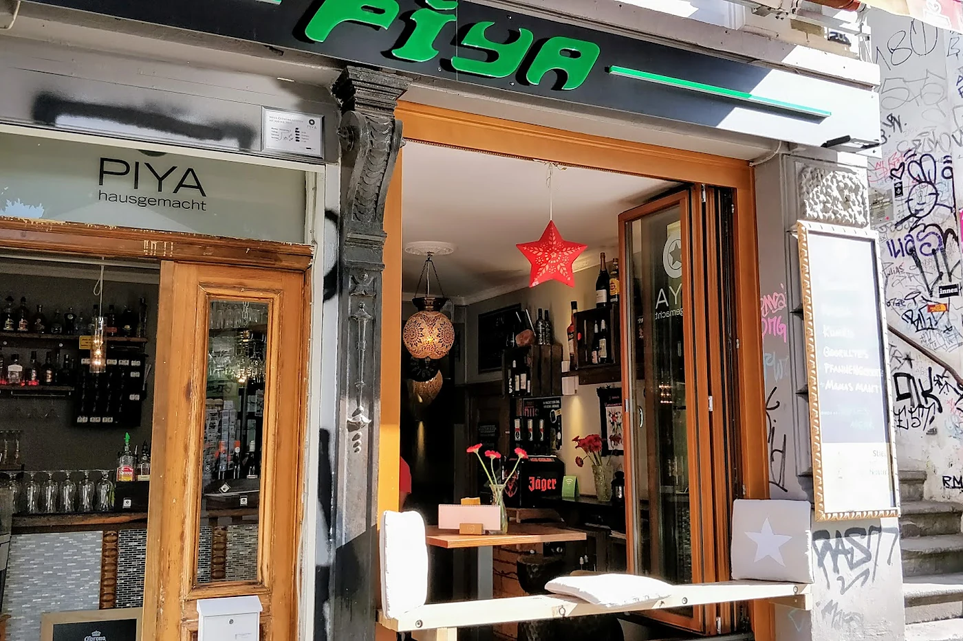 Eingang des Nosh in der Susannenstraße mit grüner Piya-Leuchtschrift, offener Tür und Sticker-Wand