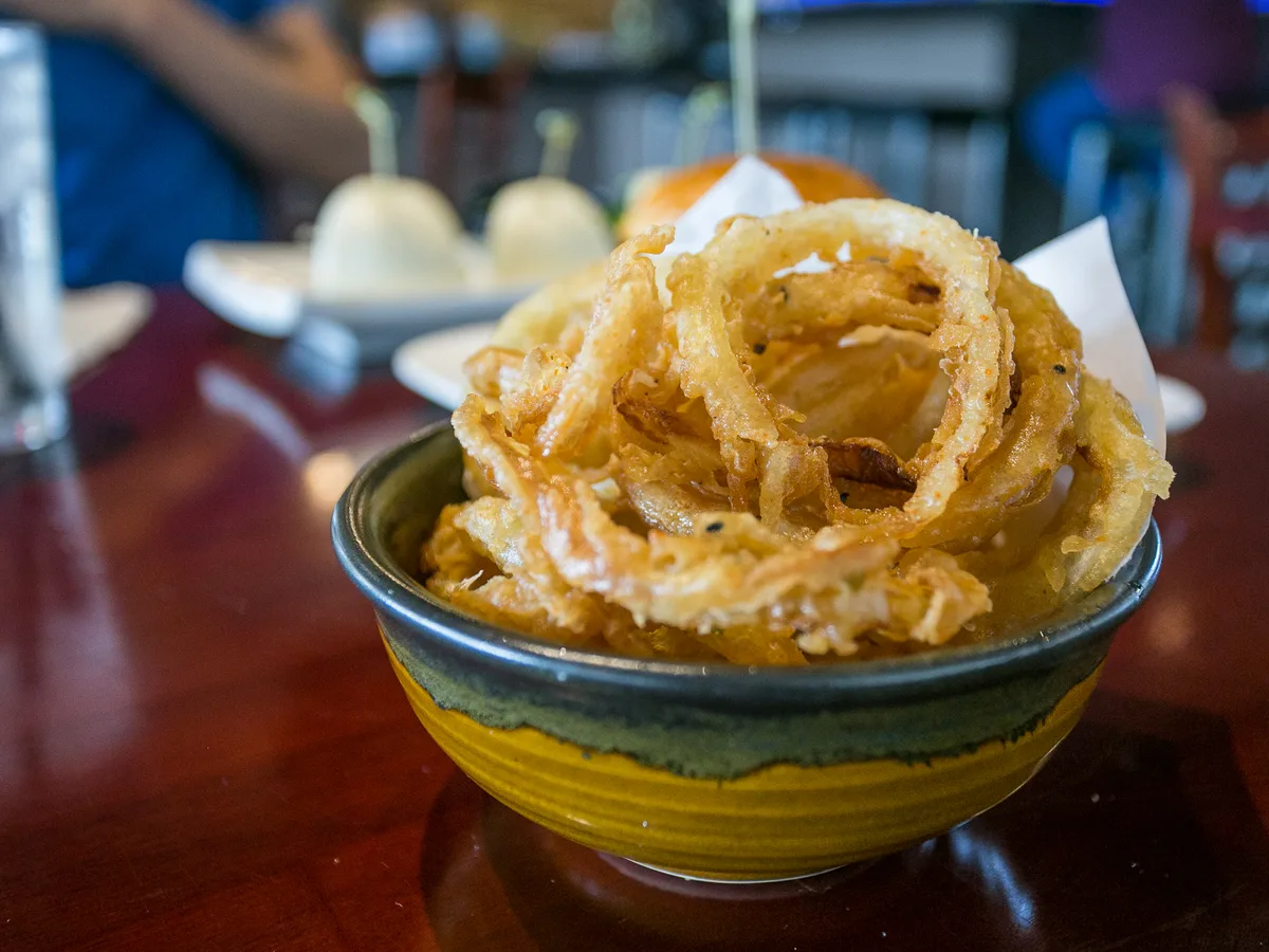 Ein Turm aus knusprigen Zwiebelringen in einer Schüssel, im Hintergrund die Bar