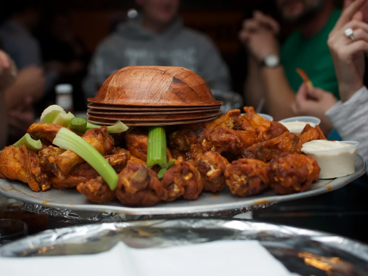 Großer Teller Buffalo Wings mit Sellerie und Dip in geselliger Sportsbar-Runde