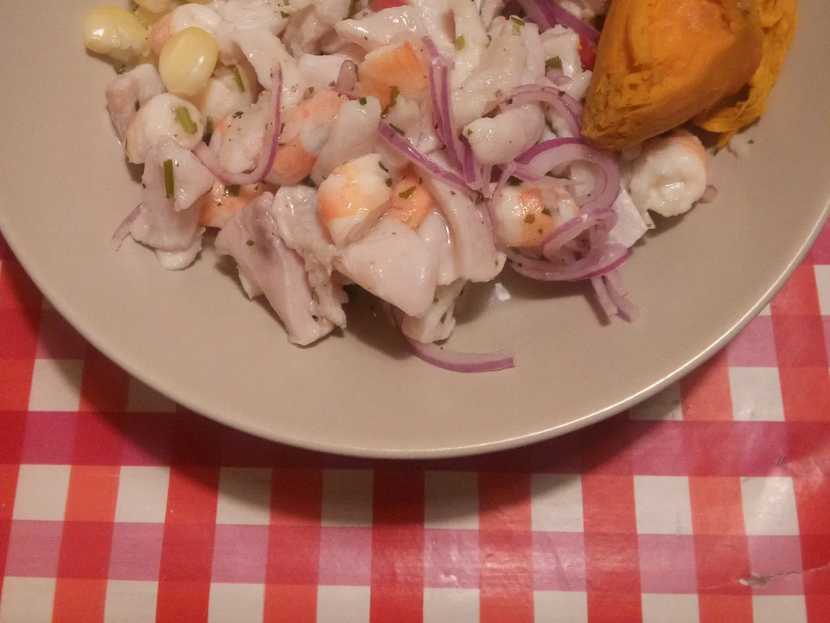 Ceviche mit Fisch, Garnelen, roten Zwiebeln, Choclo und Süßkartoffel auf einem Teller
