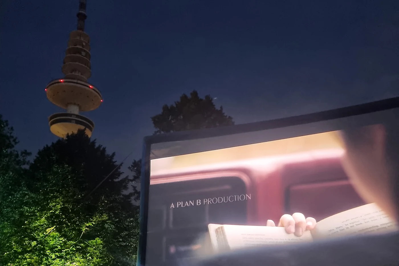Beleuchtete Kinoleinwand bei Nacht zwischen Parkbäumen, links der angestrahlte Heinrich-Hertz-Turm