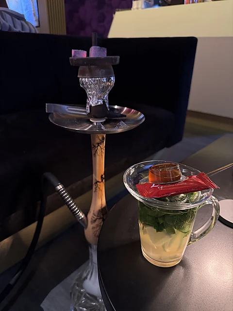 Wasserpfeife mit Glaskopf und Holzrauchsäule auf einem Tisch, daneben ein Glas hausgemachte Limonade mit Minze