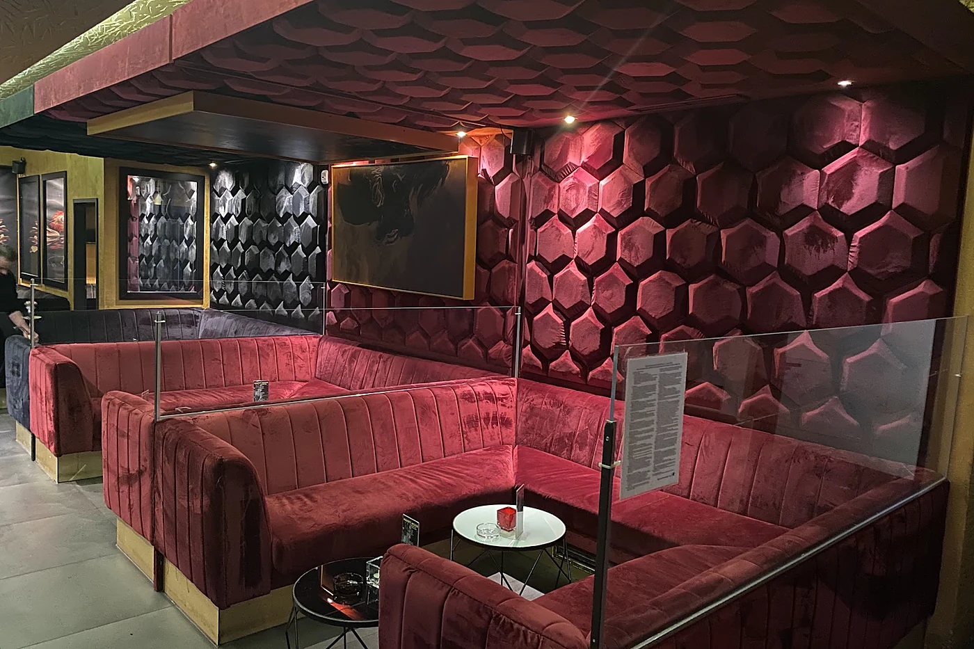 Lounge mit roten Samtsofas, Wänden aus Wabenpolstern, goldener Decke und einem kleinen runden Tisch